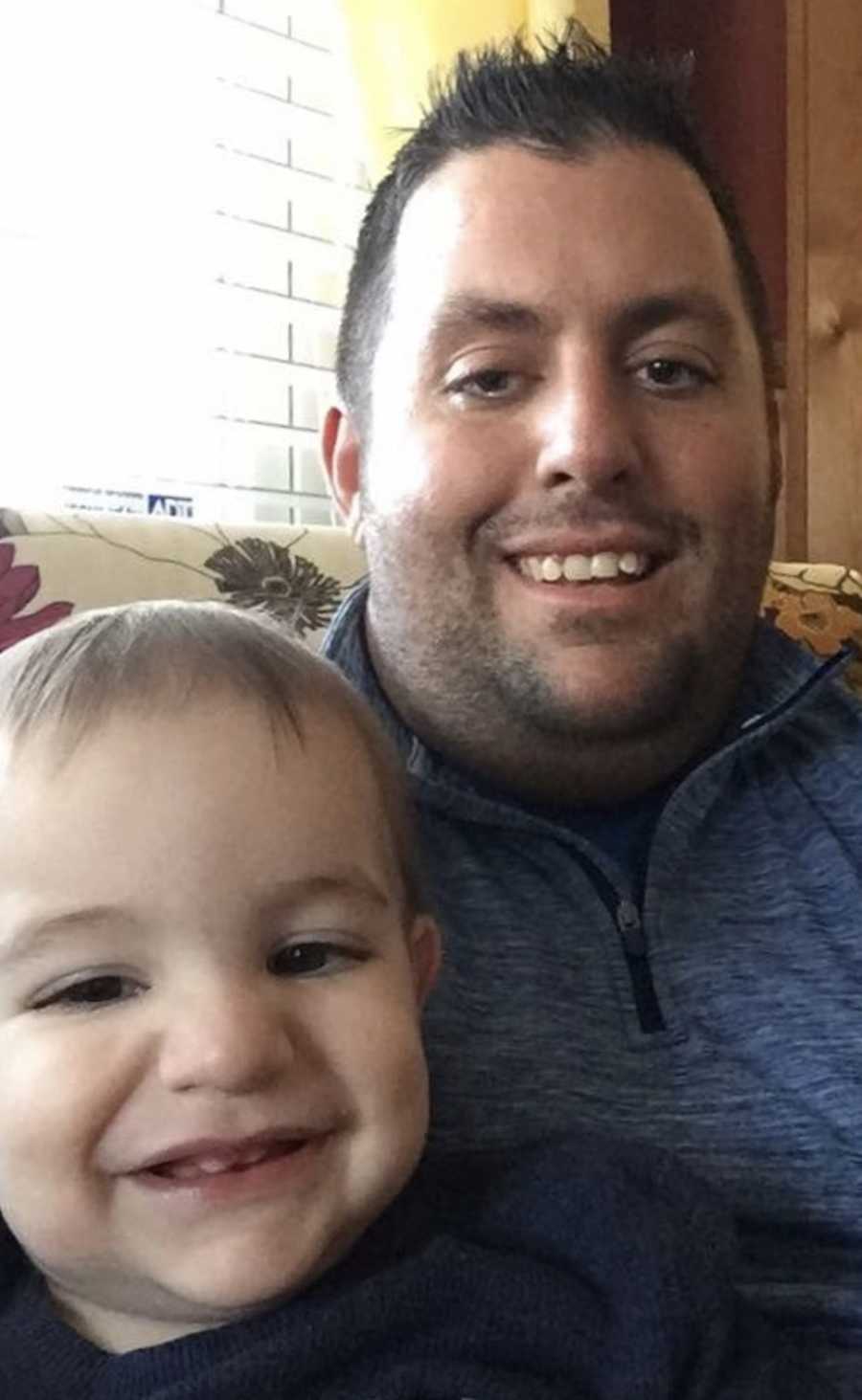 Father sits on couch smiling in selfie with toddler who has Febrile Seizures