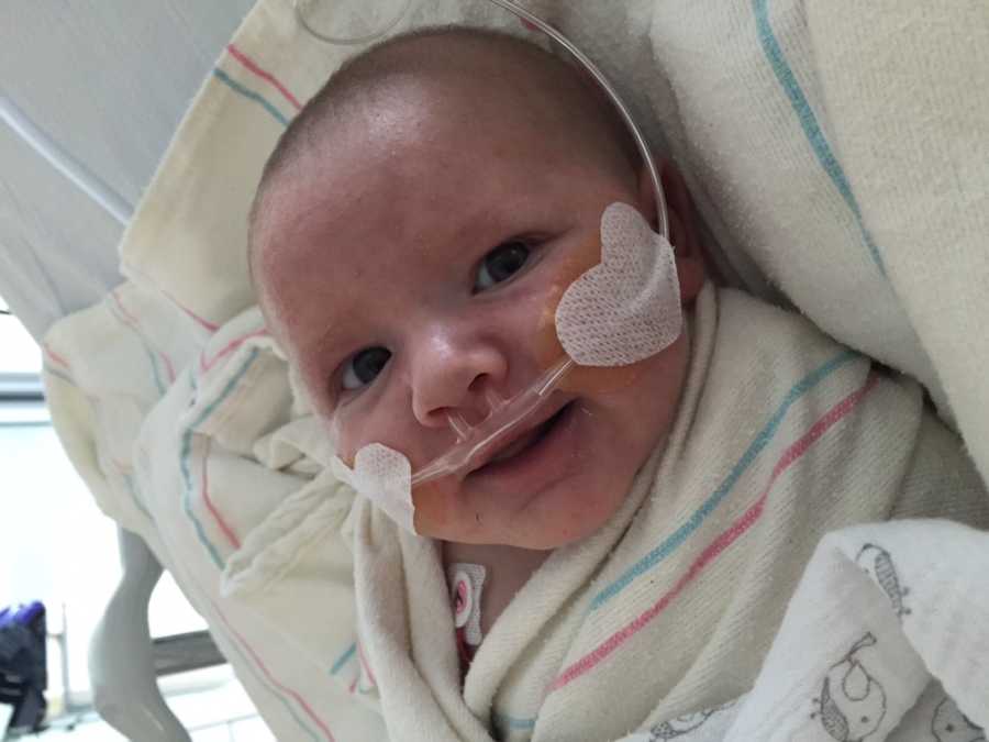 Infant in hospital bed smiling with oxygen up his nose