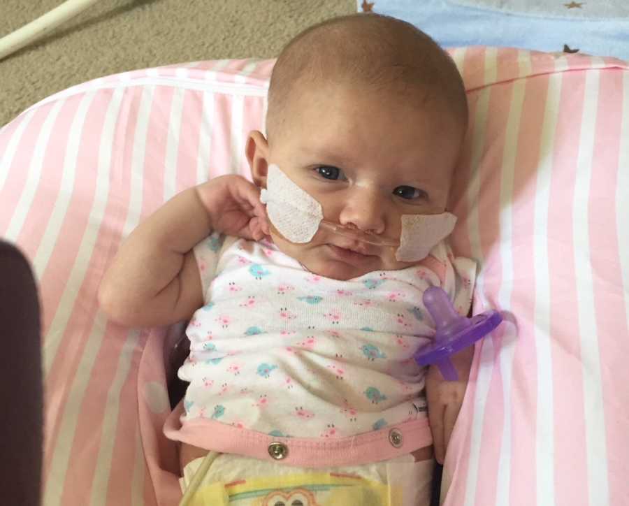Newborn who had open heart surgery lays on pink and white stripe pillow with oxygen tube
