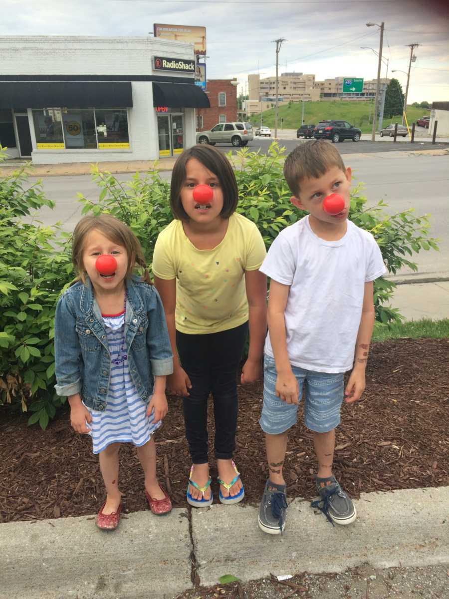 Three children standing in parking lot with red clown noses on their nose