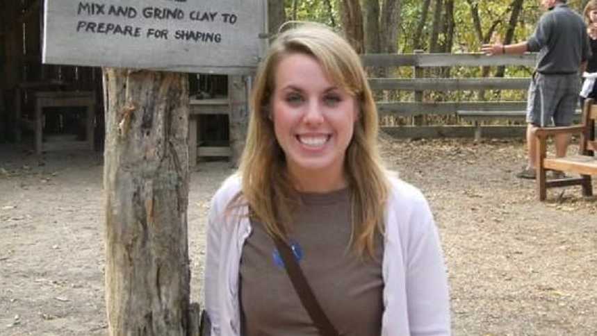 Woman who was in abusive relationship stands smiling beside wooden post with sign on it