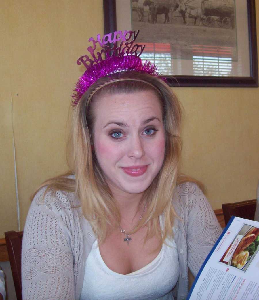 Woman who was in abusive relationship smiles at restaurant table wearing pink happy birthday headband