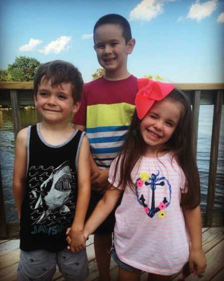 Young boy who are his parents biological son stand on porch smiling behind his two foster siblings