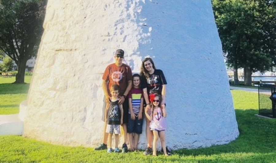 Wifes stand in front of large white structure with their biological son and two foster children