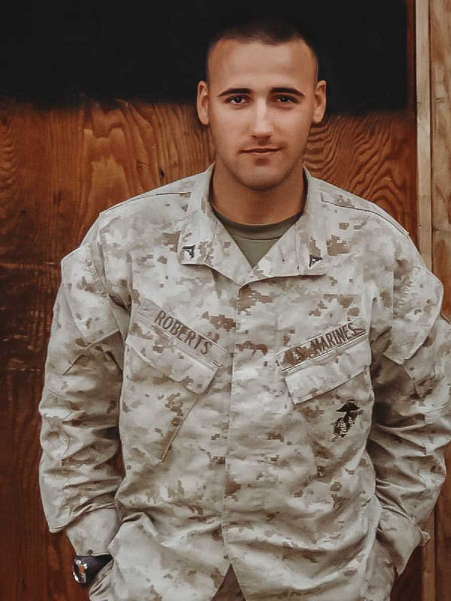 Marine stands smiling with hands in his pockets of uniform