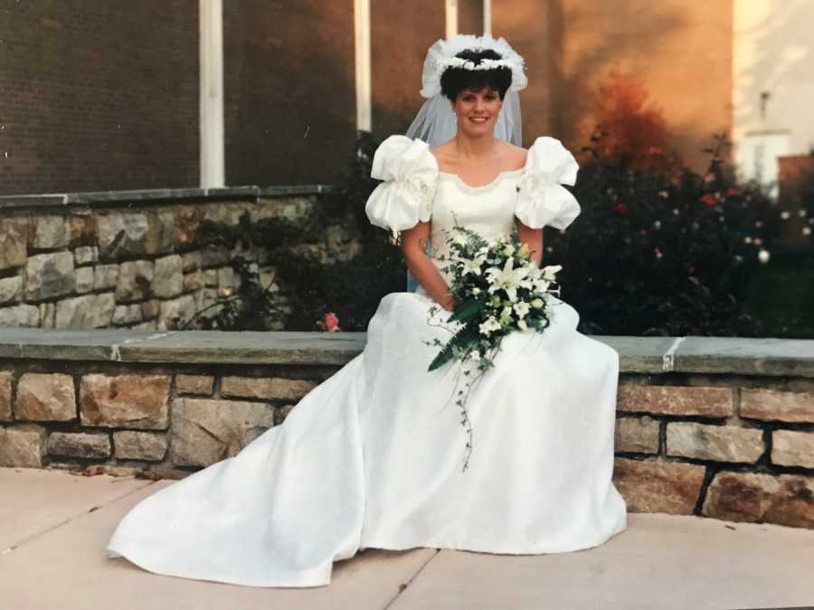 Bride sits on stone wall holding bouquet of white flowers