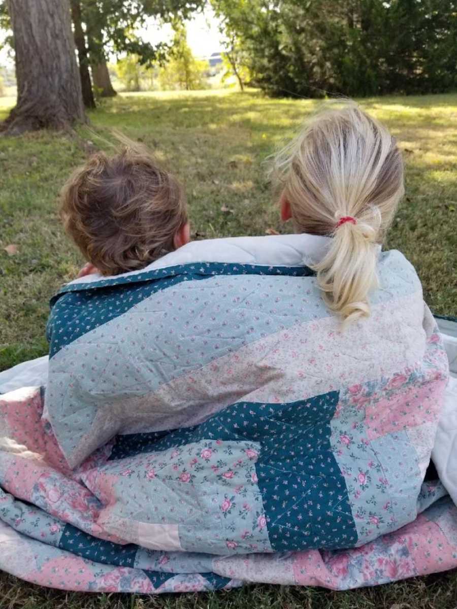 25 year old quilt wrapped around children sitting on ground outside