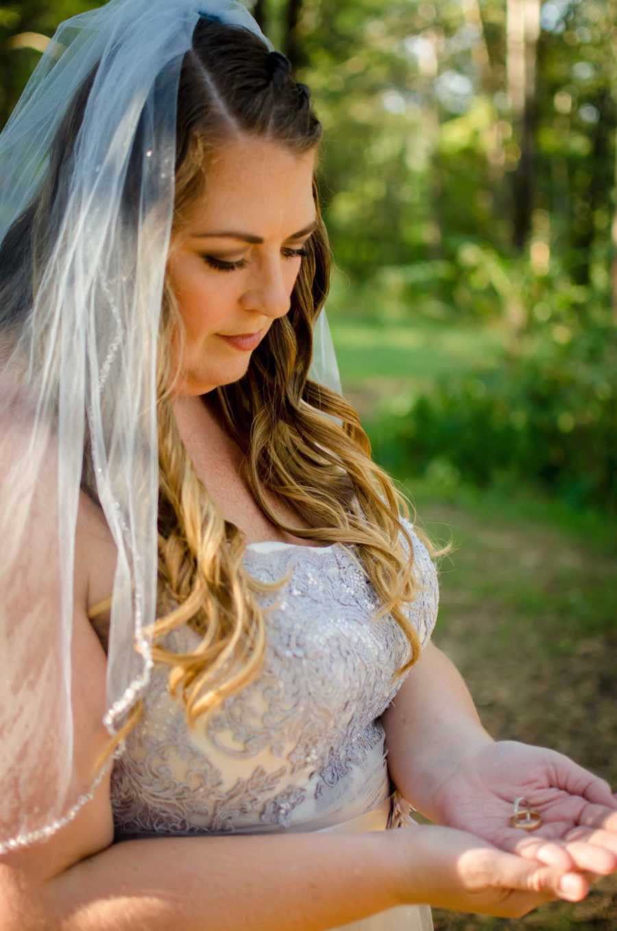 Close up of woman in wedding gown looking down at her hands where she holds her deceased husband's wedding ring