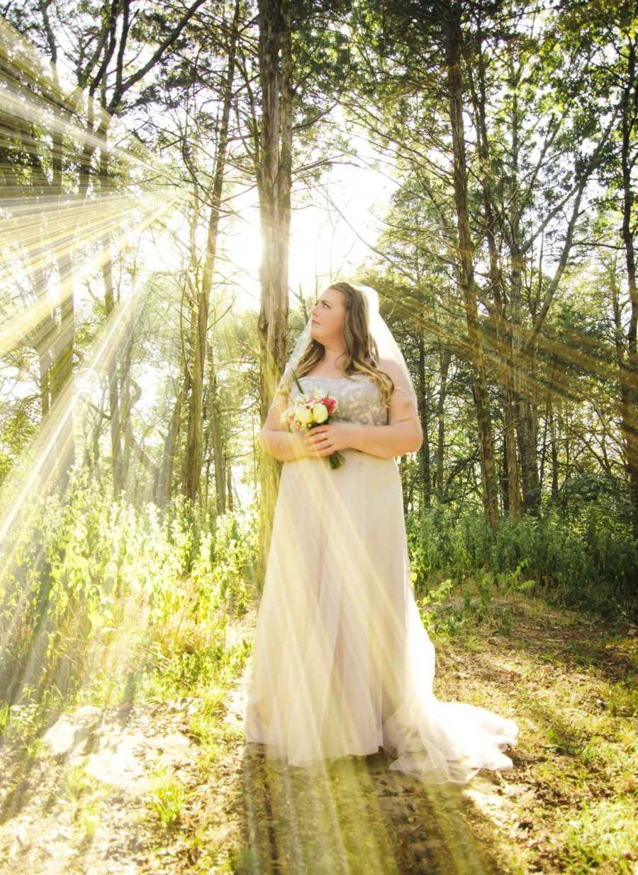 Woman stands in wedding gown in forest looking up to the side