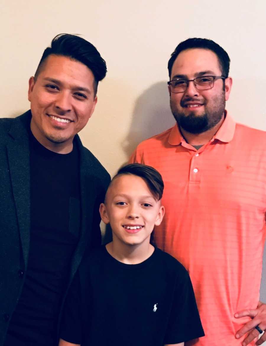 Young boy stands smiling with dad and stepdad