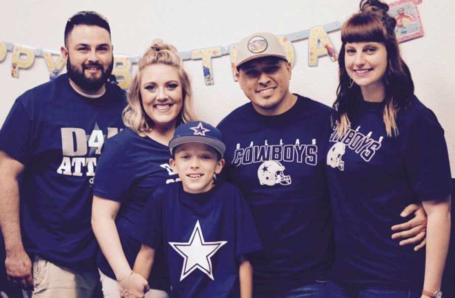 Young boy stands smiling in front of his mom and dad and their new spouses who are all wearing Dallas Cowboy clothes