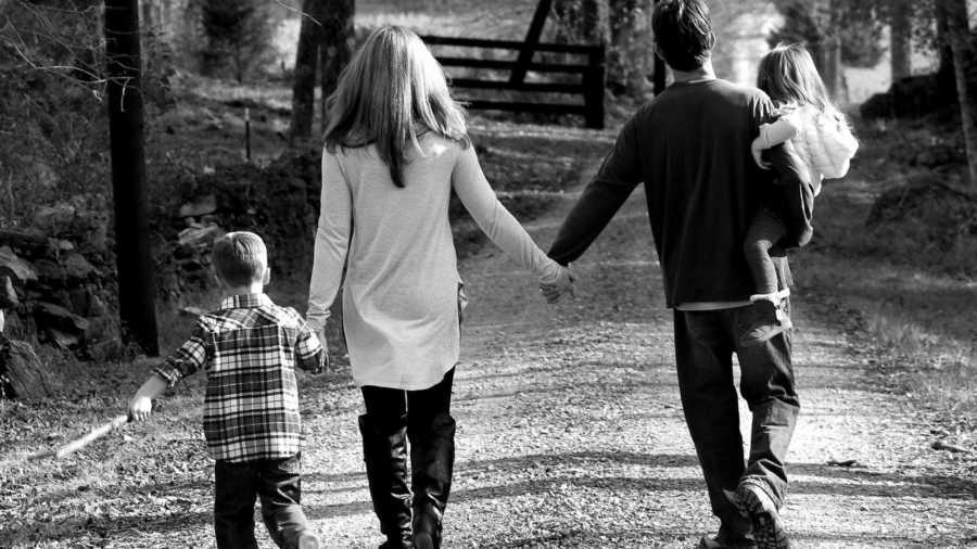 Husband and wife who are very similar walk down path holding hands while mother holds sons hand and father holds daughter