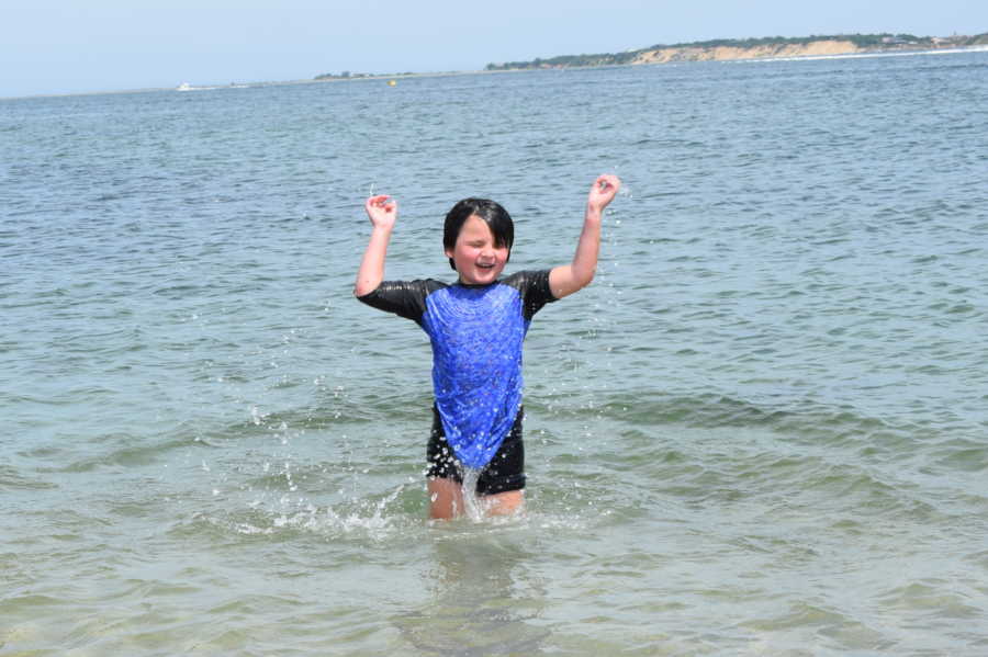 Transgender child smiling in body of water with hands in the air