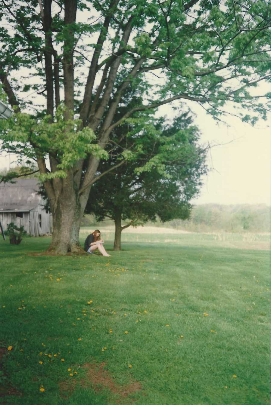 Woman who has experienced a lot of loss in her life sits out side leaning against tree
