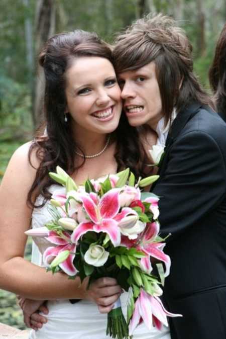 Bride smiles holding bouquet of lily's while husband stands hugging her from the side