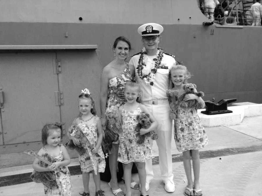 Woman stands beside military husband with their four daughters standing in front of them