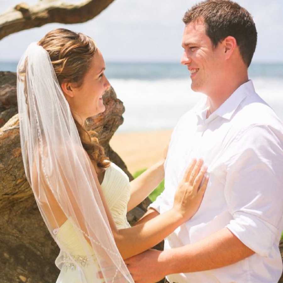 Bride and groom stand smiling at each other at beach wedding