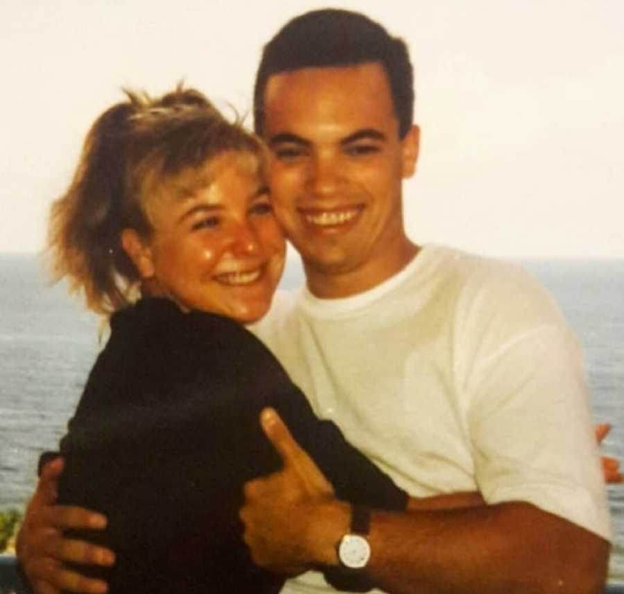 Man smiles hugging fiancee who has since passed with body of water in background