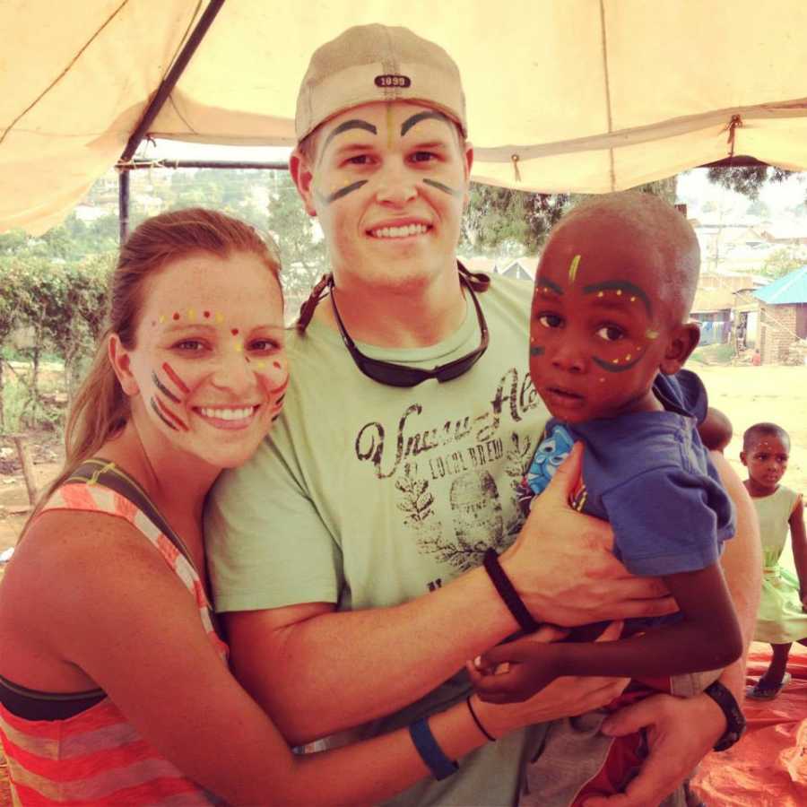 Husband and wife with face paint on stand holding orphan in Uganda 