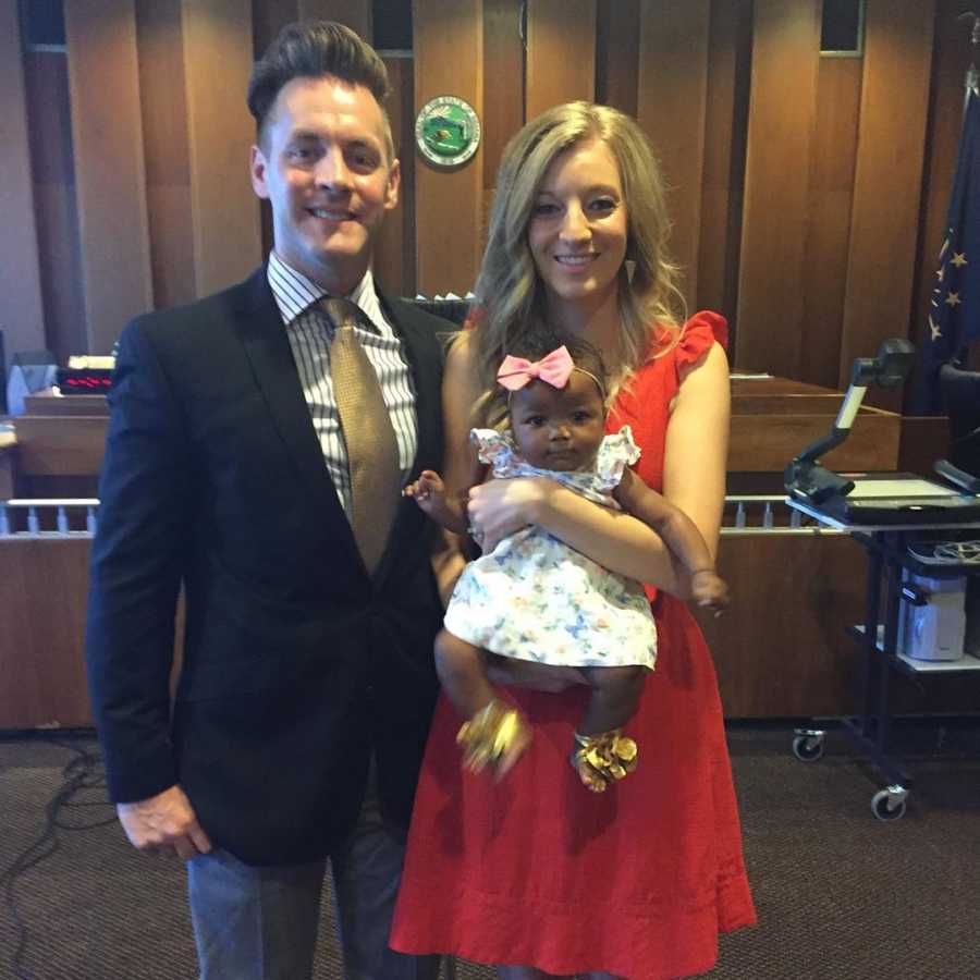 Husband stands beside wife who is holding their adopted baby in adoption court