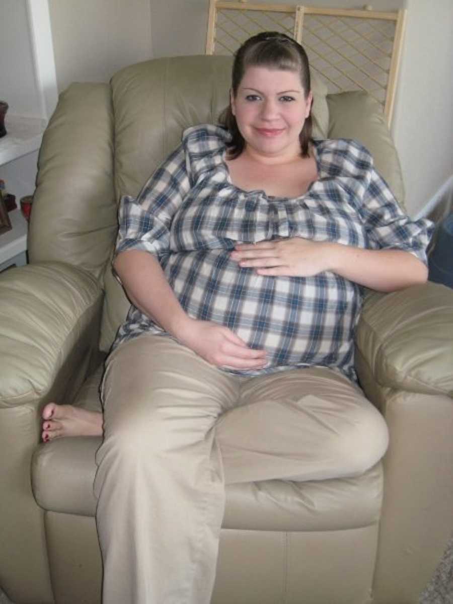 Pregnant woman sits in chair in home holding her stomach smiling
