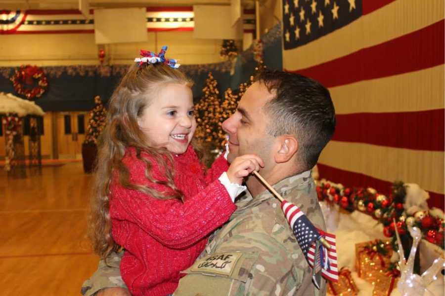 Army father stands in gymnasium holding toddler who has had a lot of medical issues
