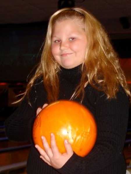 Overweight teen smiles while holding orange bowling ball