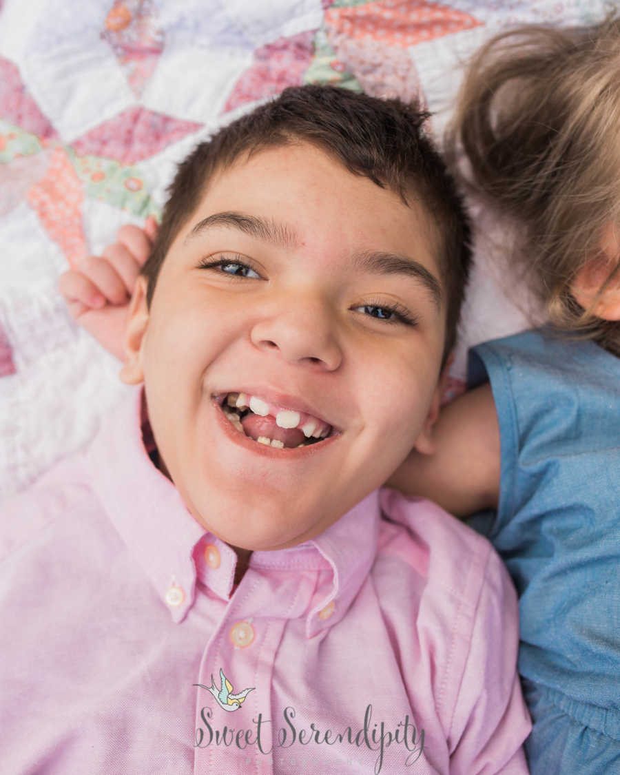 Young boy with shaken child syndrome smiles as he lays on blanket beside young girl