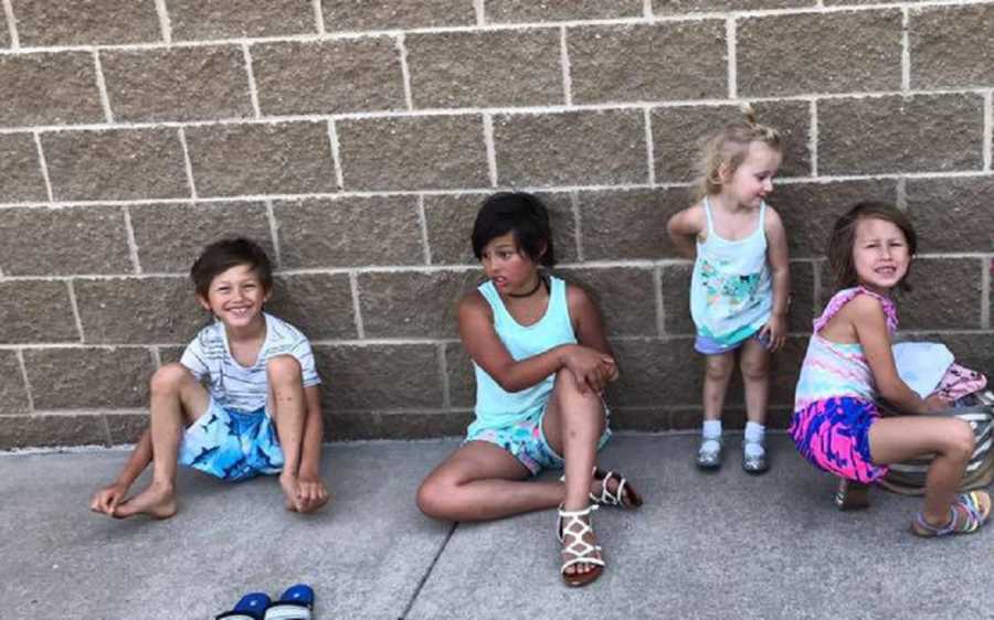 Four foster children sitting on ground leaning against brick wall