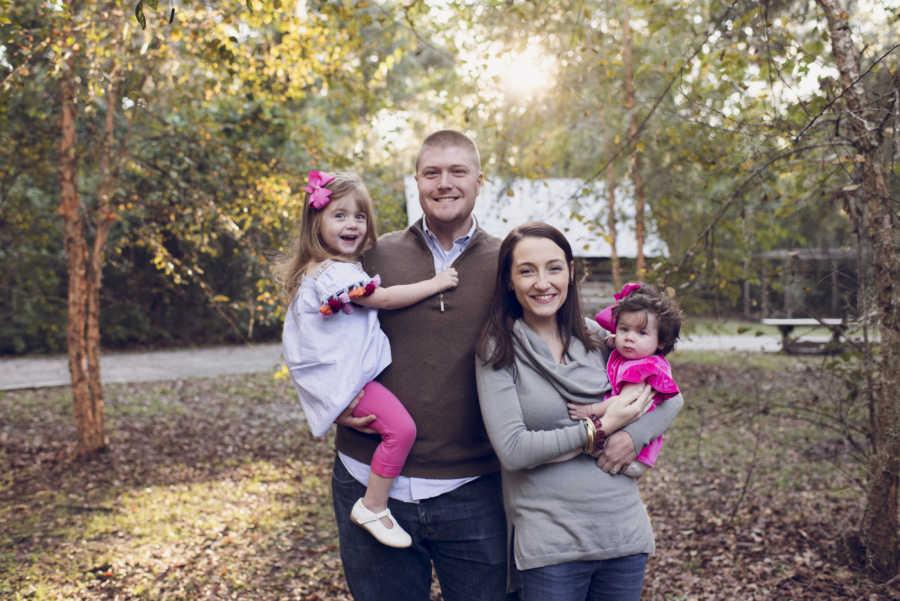 Husband and wife stand outside holding their biological daughter and adopted daughter