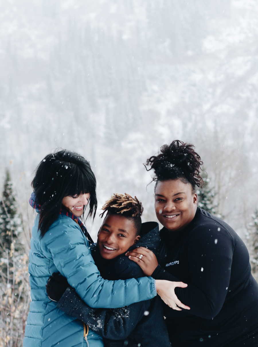 Son stands in group hug with birth mother and adopted mother outside in snow