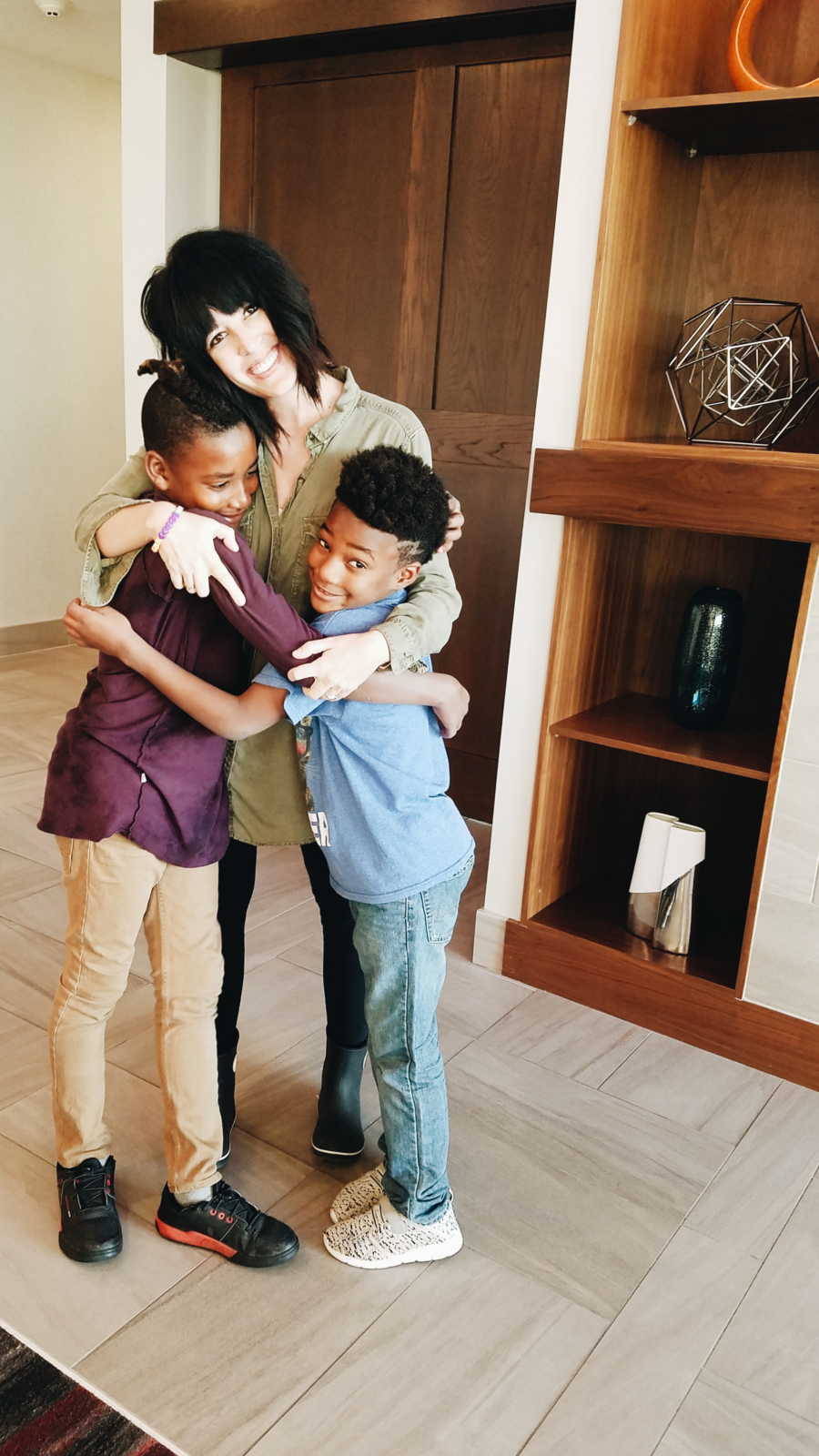 Mother stands in home hugging adopted son and his biological brother