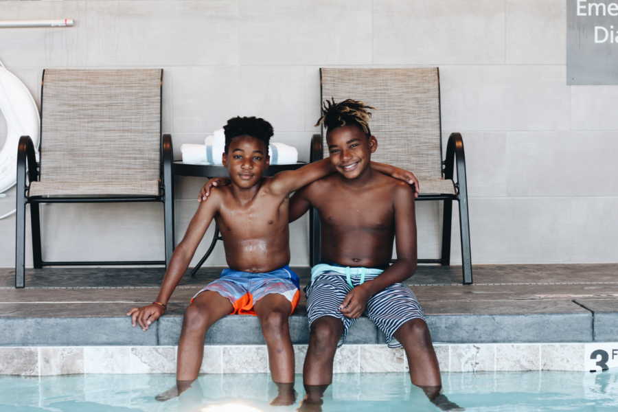 Young boy who was adopted at birth sits on indoor pool deck beside biological brother