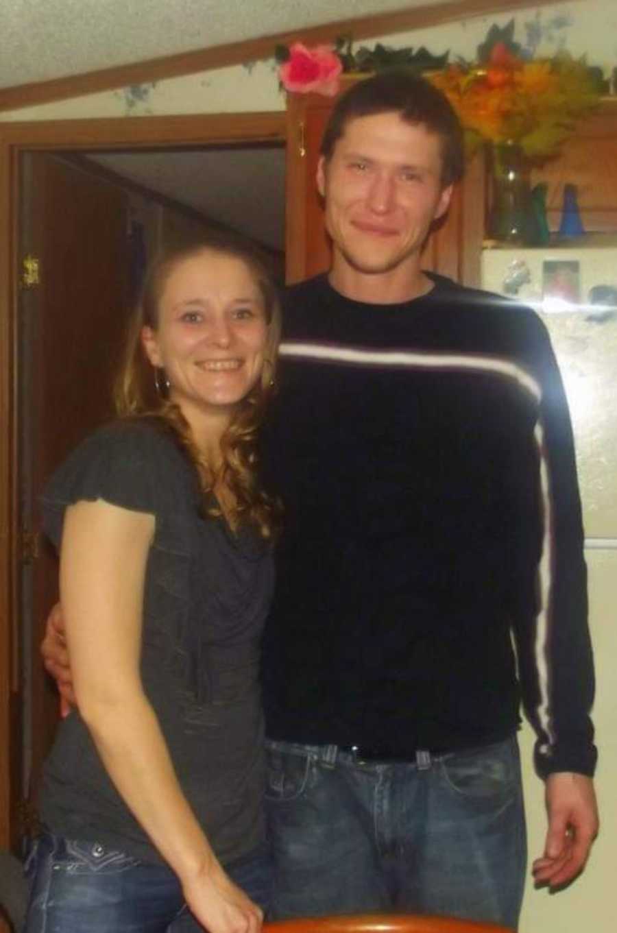 Brother and sister stand in kitchen with arms around each other smiling