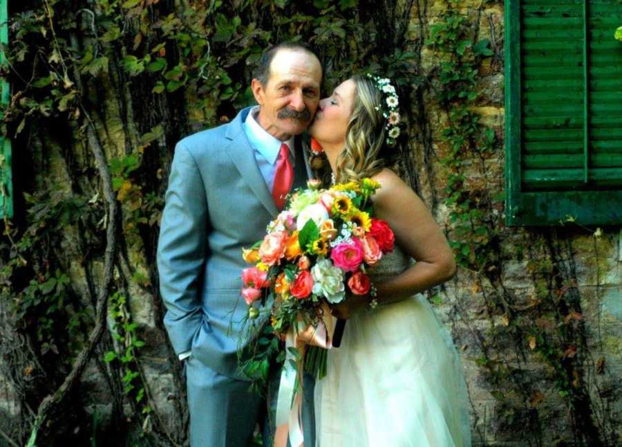 Bride holding bouquet of colorful flowers kissed father on cheek