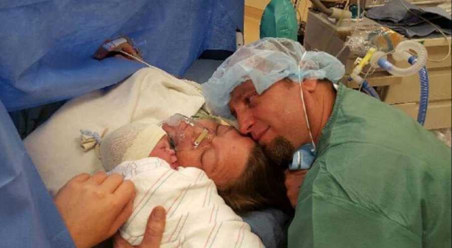 Mother who had c-section lays in operating room while husband holds newborn with down syndrome beside her