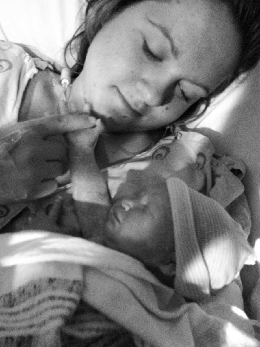 Mother lays beside newborn holding her hand while she sleeps
