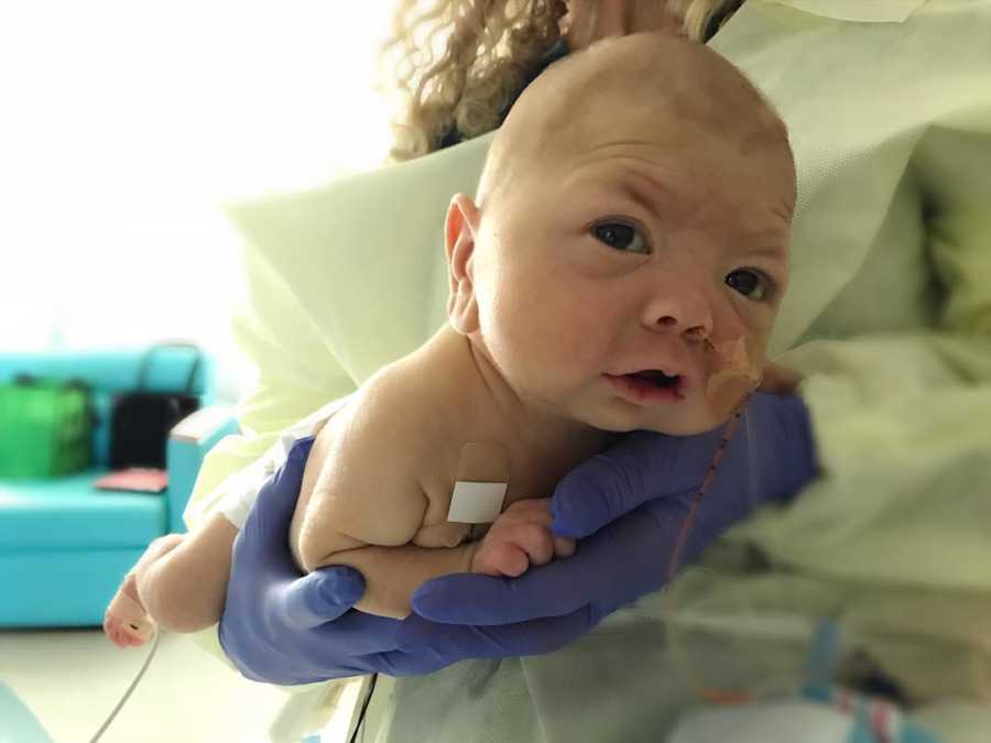 Newborn with HLH being held in hands of nurse with purple gloves on 