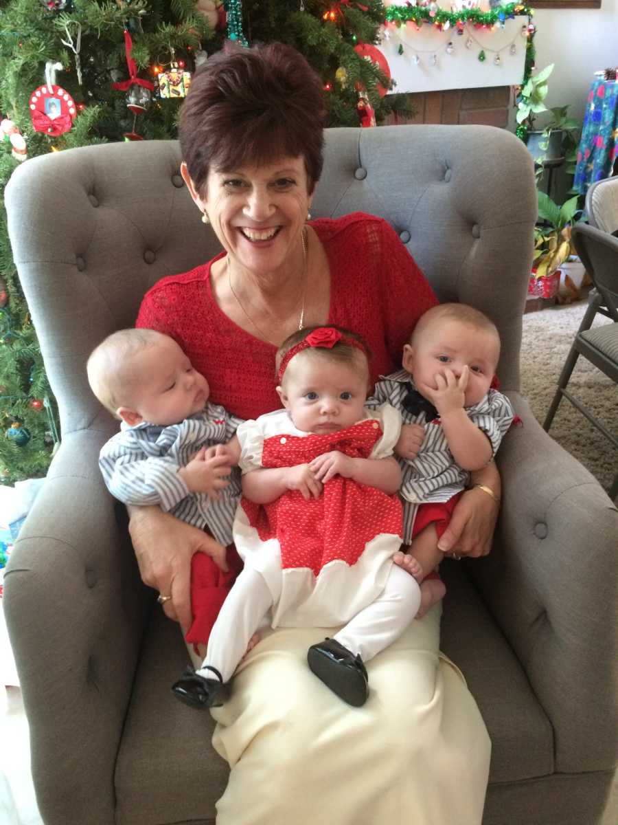 Grandmother sits in chair with triplets in her lap dressed for Christmas