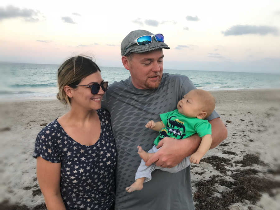 Father holds son with HLH in one arm with other wrapped around his wife on beach