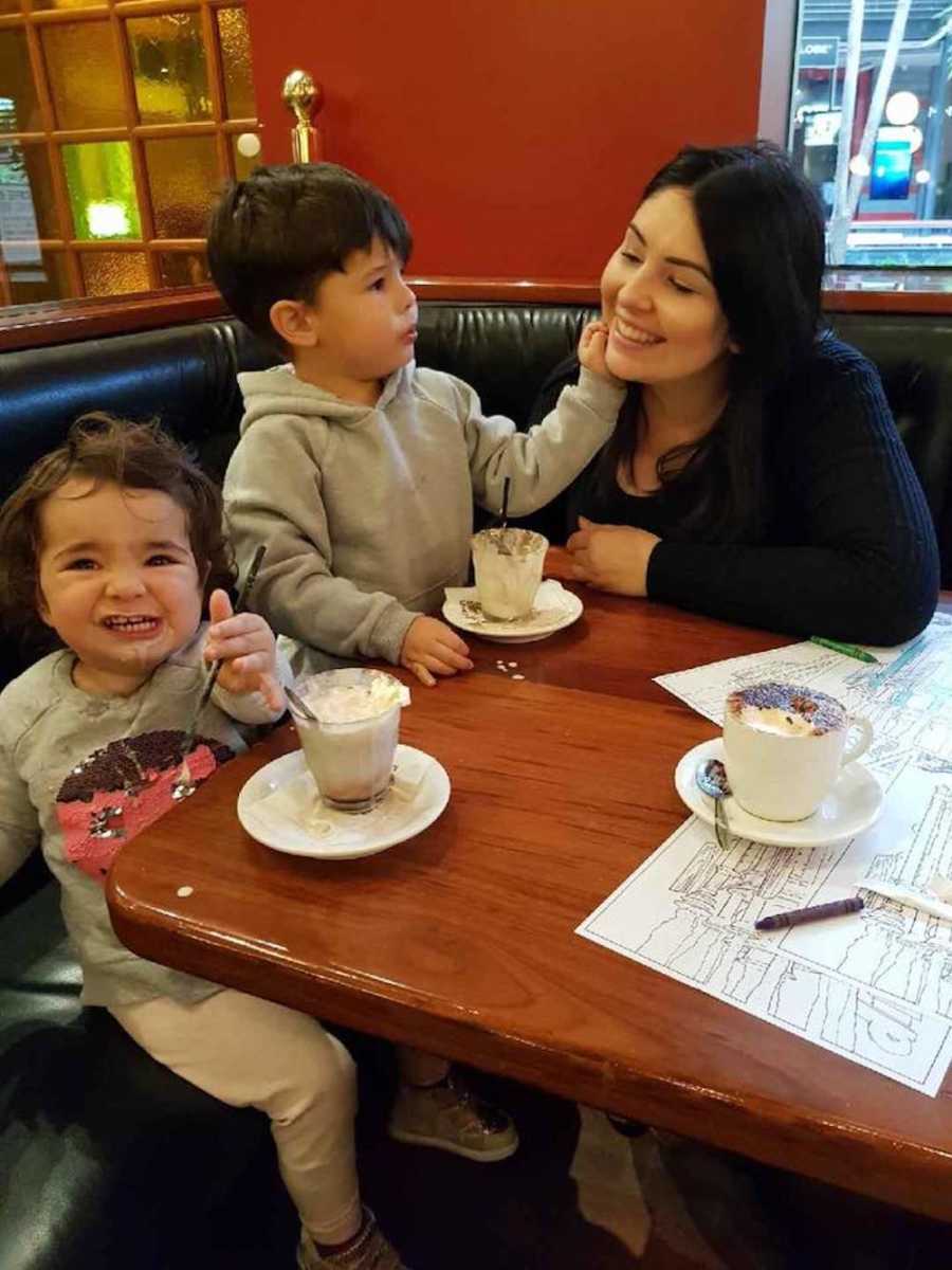 Mother sits at restaurant table with young son and daughter who eat ice cream