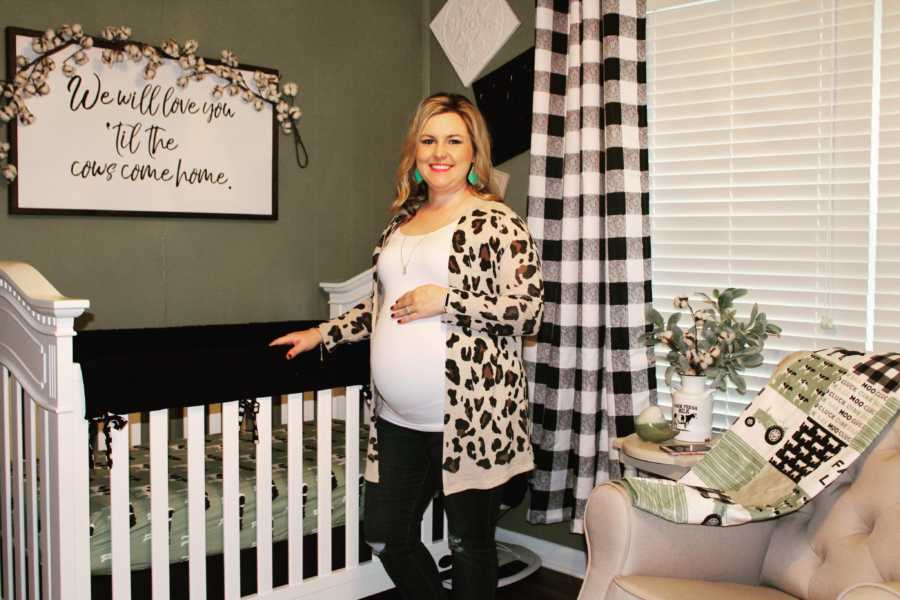 Woman who struggled with fertility is pregnant standing beside crib in baby's nursery