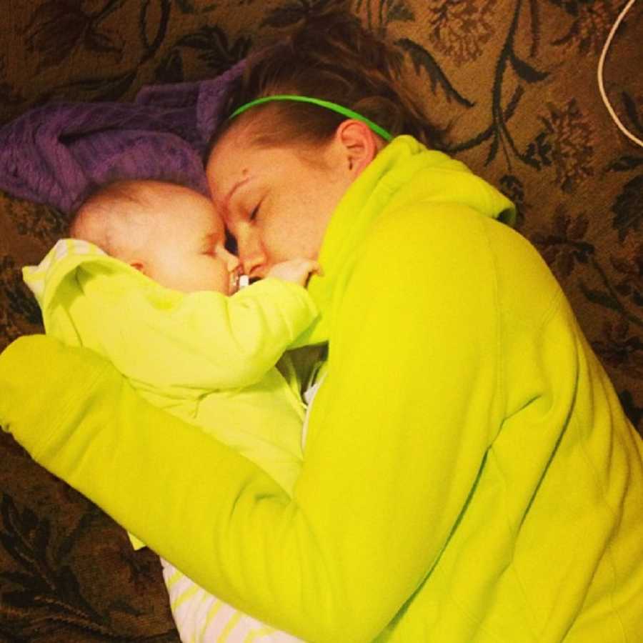 Mother asleep on couch holding onto her baby who sleeps beside her