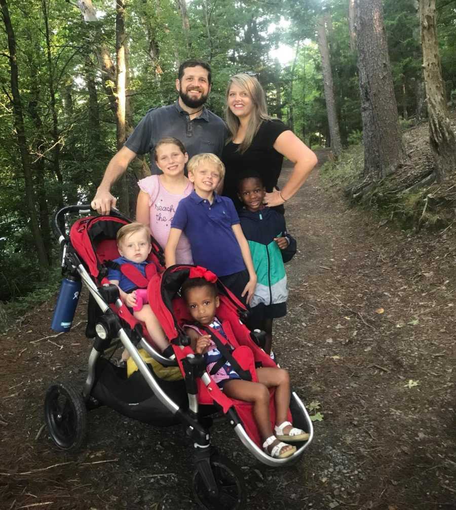 Husband and wife stands smiling on path in woods with their five children