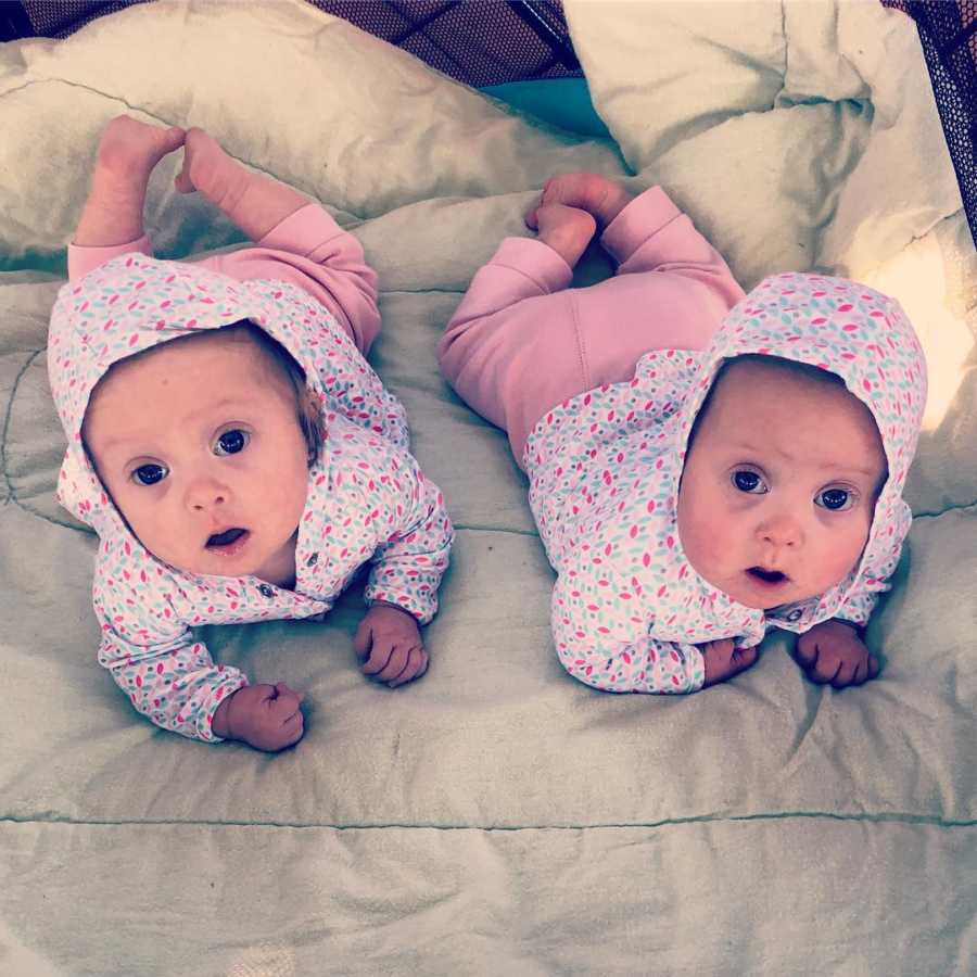 Twin girls lay on their stomachs looking up in matching outfits