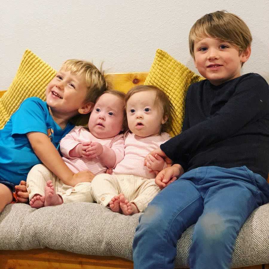 Twin girls with down syndrome sit on couch with their two older brothers on either side of them