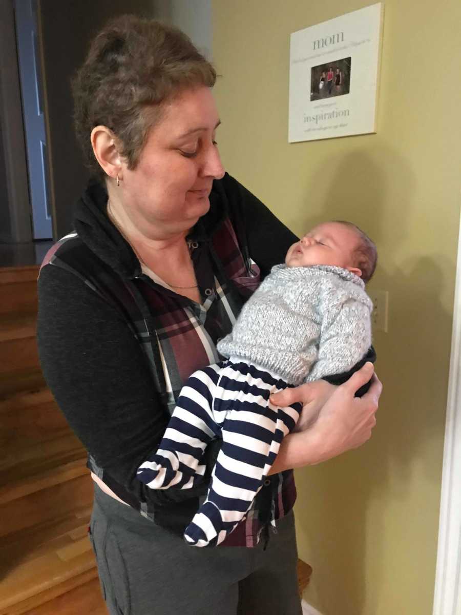 Woman with cancer stands in home holding grandson in her arms