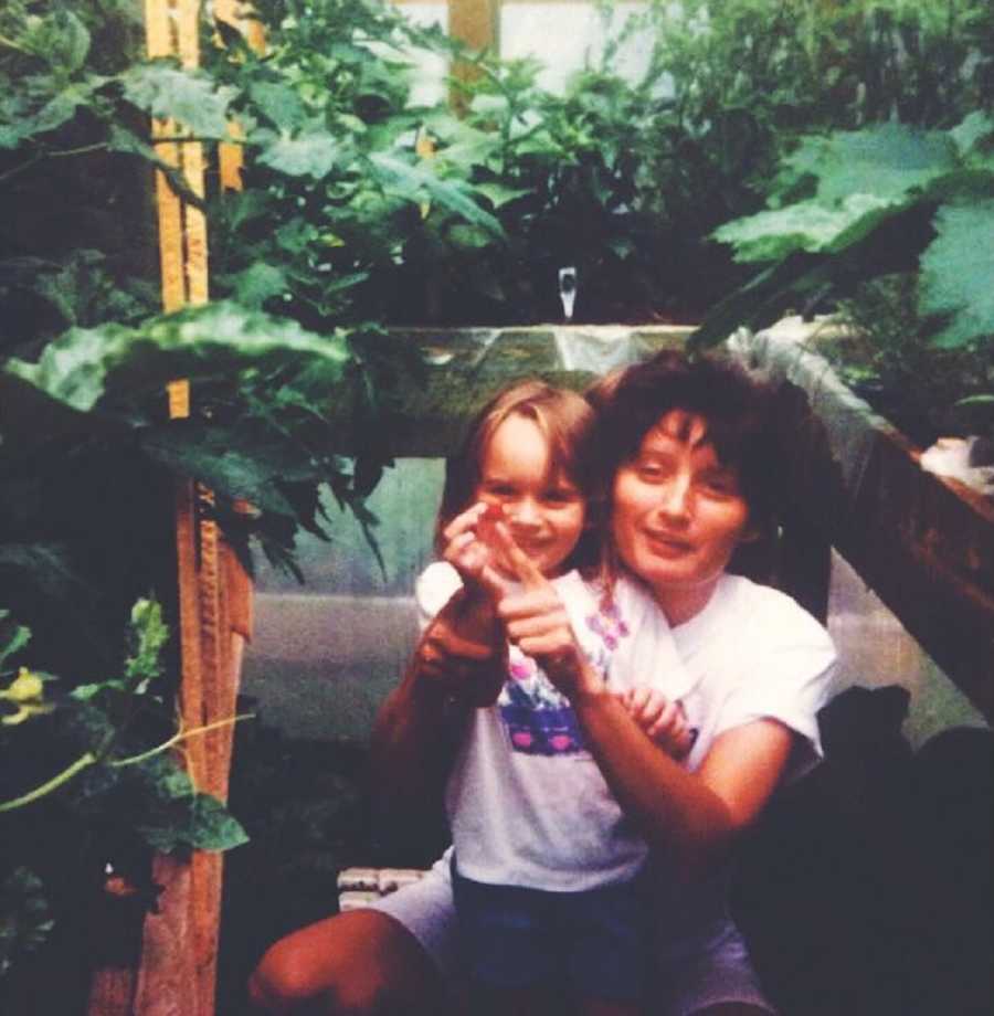 Mother squats behind young daughter in plant nursery