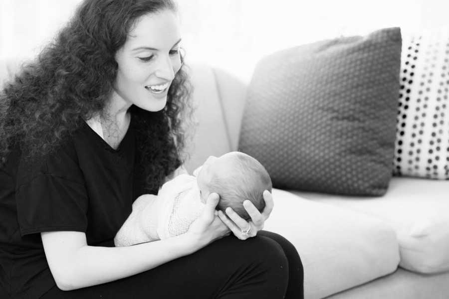 Mother who struggles with an eating disorder sits on couch smiling at baby she holds in her lap