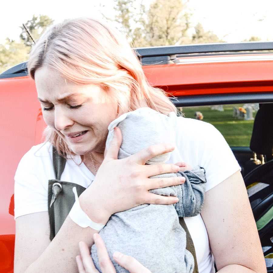 Mother cries as she holds adopted baby beside red car